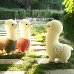 White, pink and green body alpaca plushies standing on a grass path