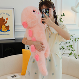 Woman hugging pink dinosaur plush pillow with heart-shaped back spikes, indoor setting with sofa and plants.