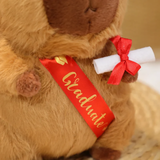 Close-up of a red Graduate sash and diploma scroll on a brown capybara plush