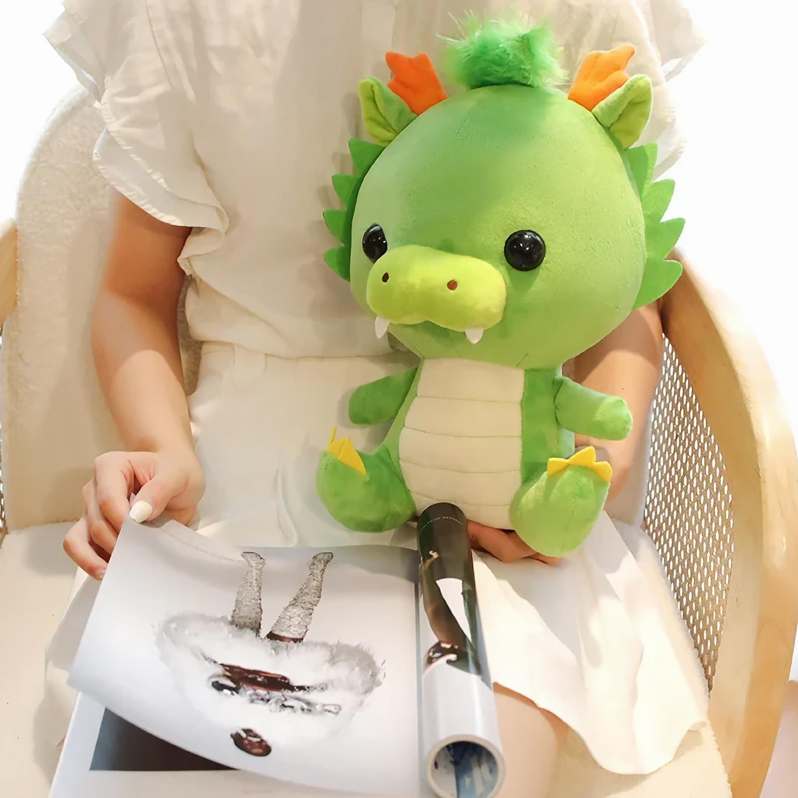 Woman seated with green dragon plush on her lap, magazine in hand.
