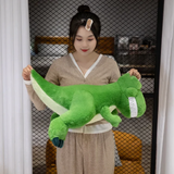 Woman holding smiling green T-Rex dinosaur plush horizontally, showing pale green belly and dark teal claws.