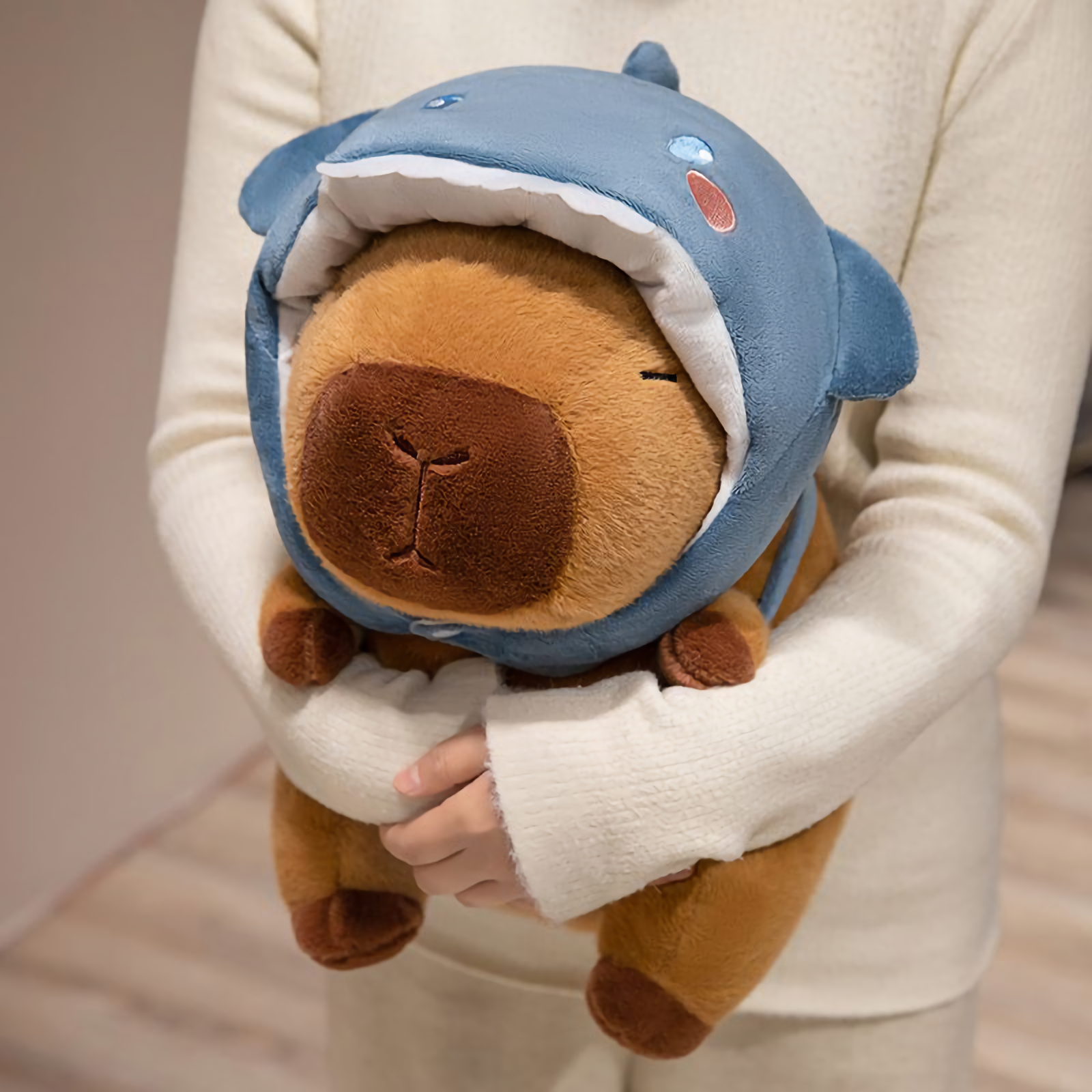 Woman hugging a capybara plush in a blue shark hood