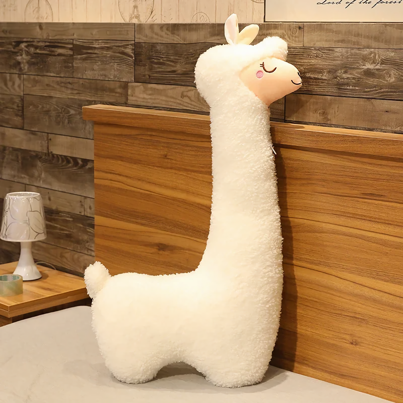 White long alpaca plush pillow standing against a wooden headboard