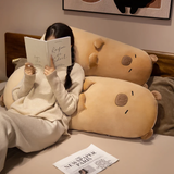 Woman reading a book on a bed beside two tan capybara bolster pillows