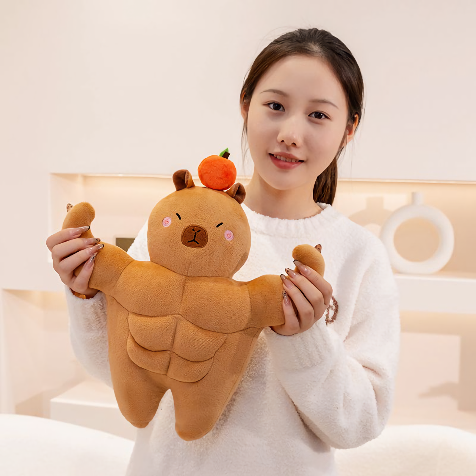 Woman smiling while holding a small muscle capybara plush with both hands