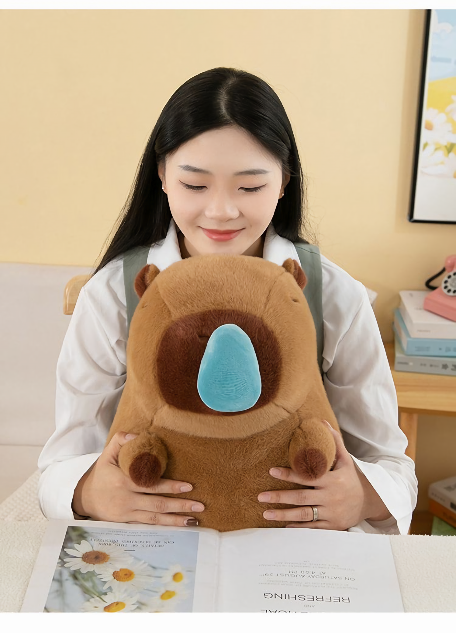 Woman looking at a brown capybara plush with a blue nose bubble on her lap