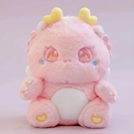 Pink fluffy baby dragon plush with sparkly star eyes and golden horns, sitting on a pink background.