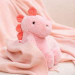 Pink dinosaur plush sitting on a soft pink blanket