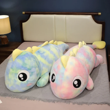 Two rainbow dinosaur plush body pillows, one blue and green and one pink, on a bed