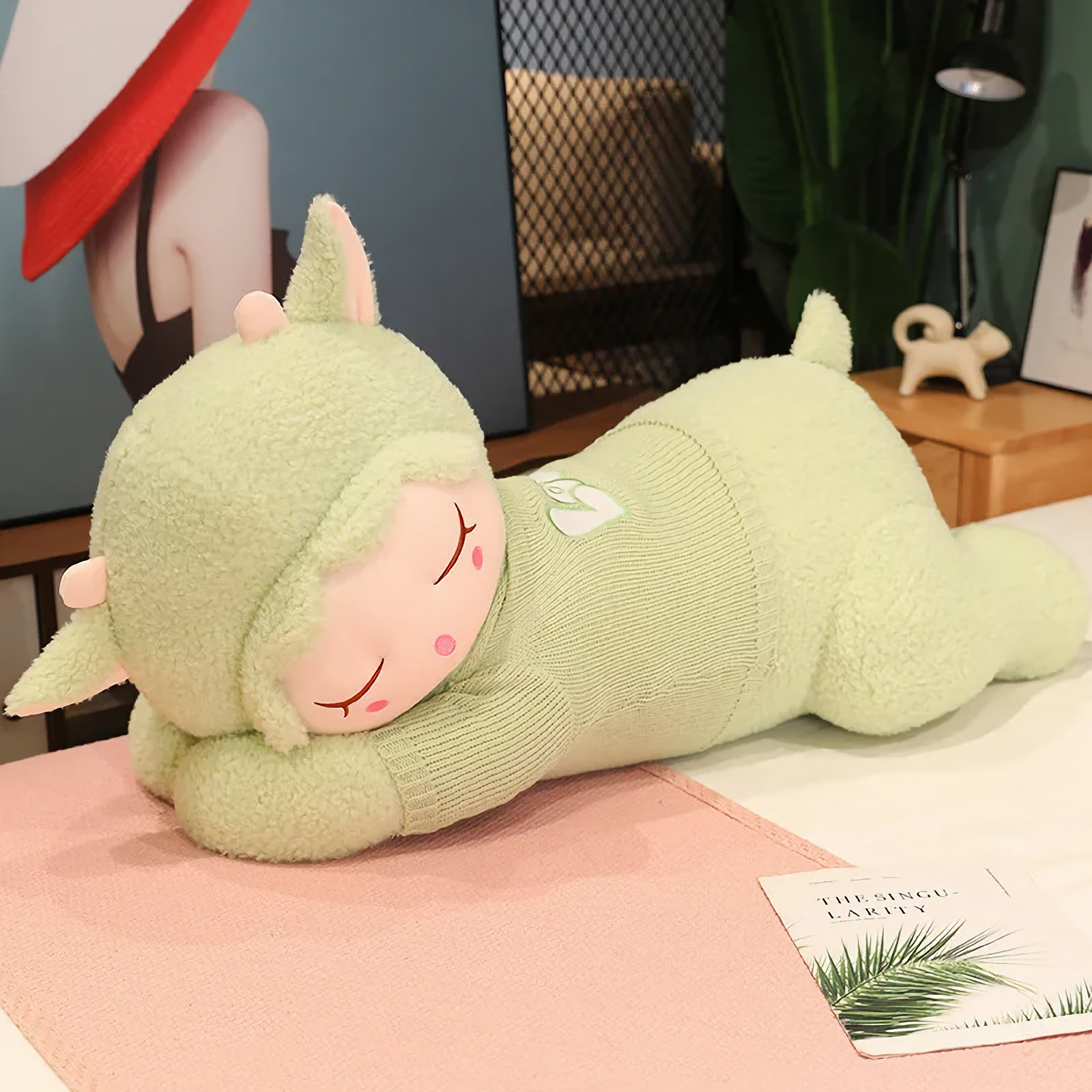 Green sleeping sheep plush pillow with a knit sweater lying on a pink blanket