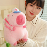 Woman smiling while holding a pink capybara plush with a white cap