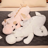Pink dragon plush and white dragon plush lying side by side on a gray bed