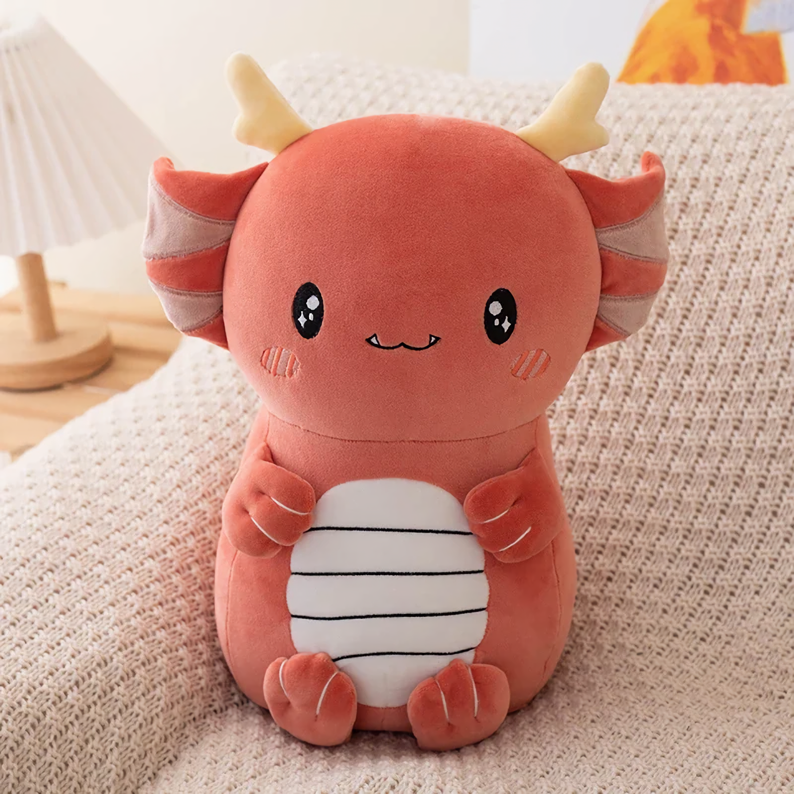 Burgundy axolotl dragon plush with cream horns, blushing cheeks and a striped belly on a sofa