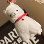 Hand holding a white alpaca plush by the ear to show its red bell collar