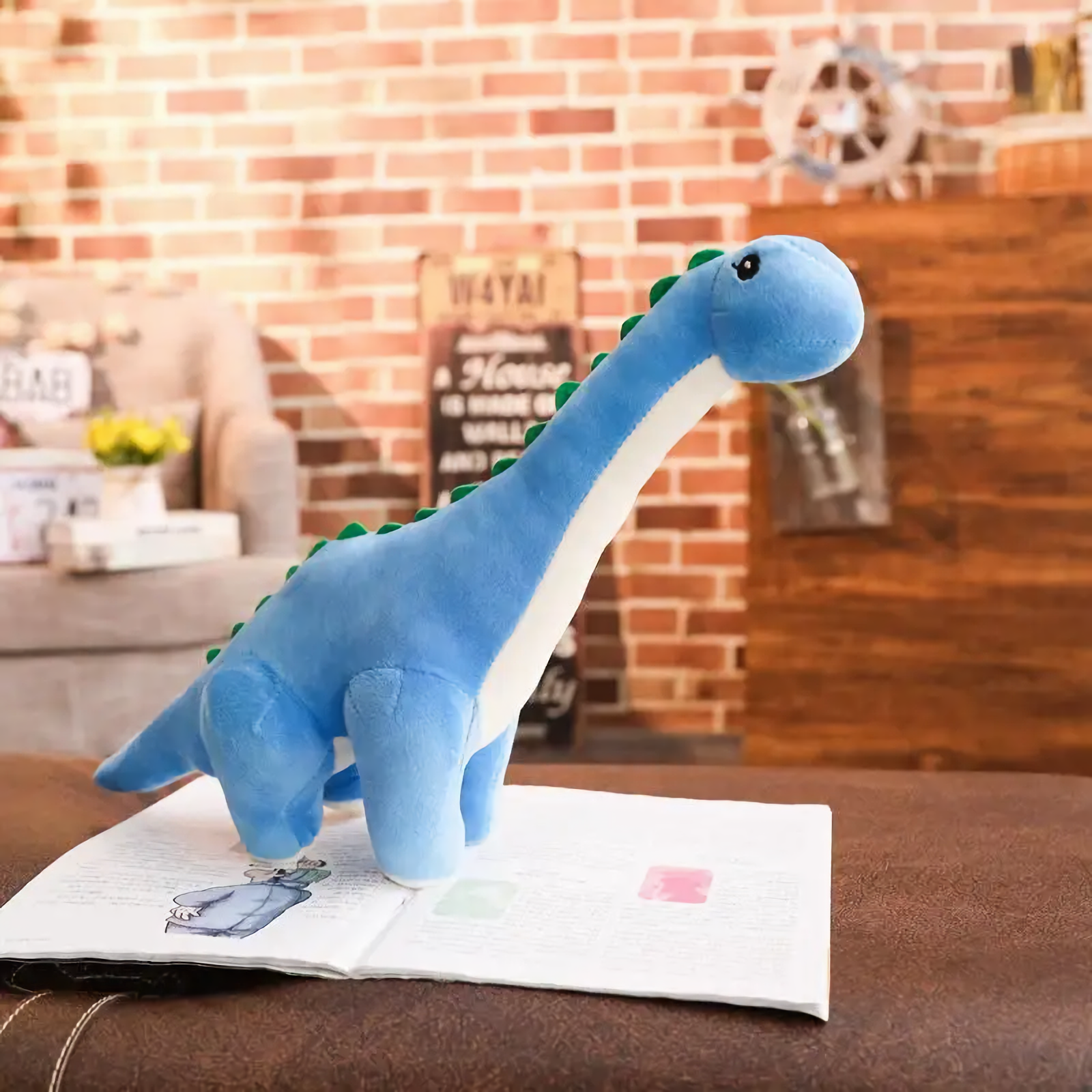 Blue Brachiosaurus plush with cream belly on a magazine in a cozy room with a brick wall background.