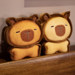 Two bread capybara plushies side by side on a wooden shelf