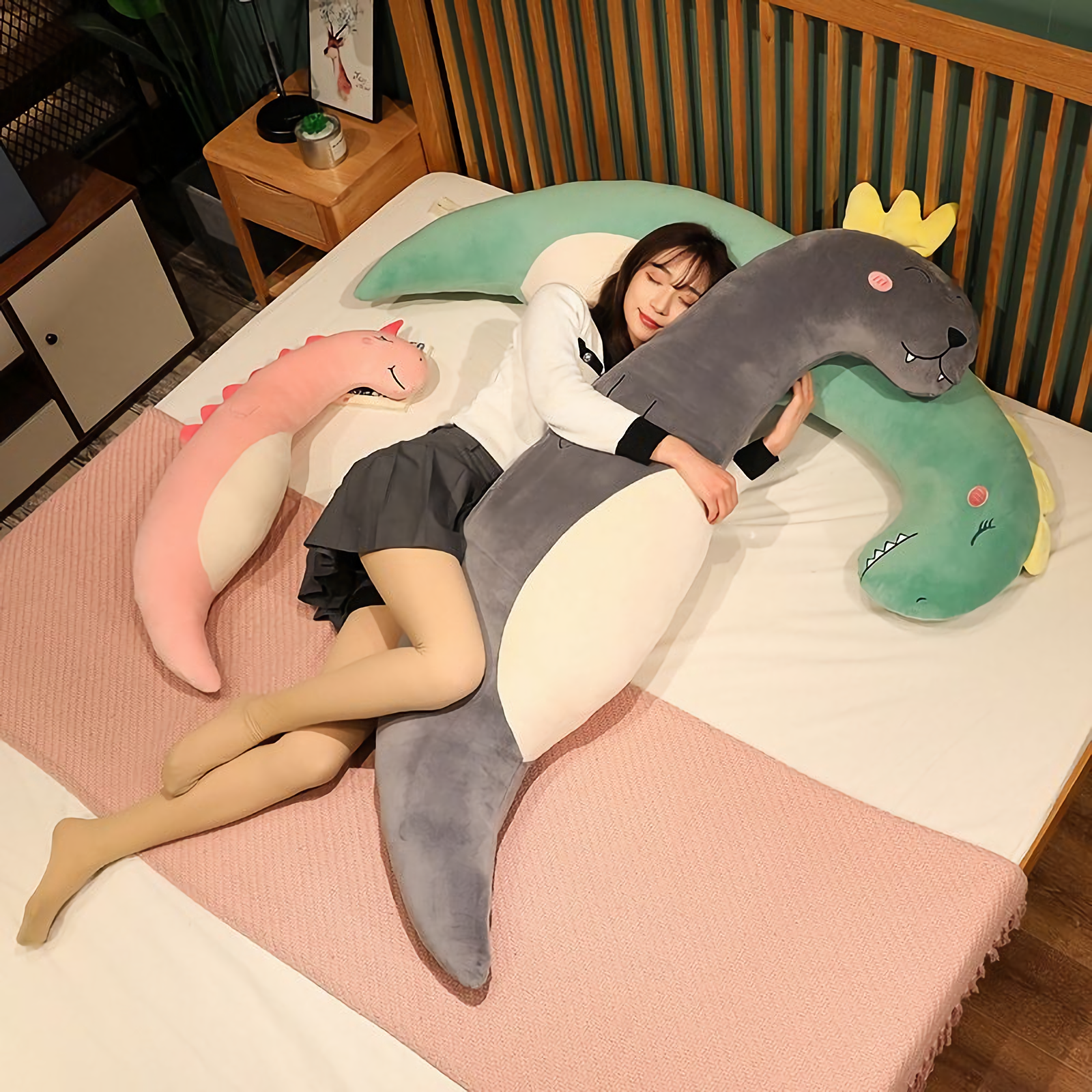 Woman lying on a bed with a curved gray sea lion plush pillow and a pink unicorn plush pillow