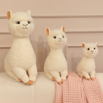 Three cream white alpaca plushies in different sizes on a sofa