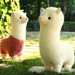 Pink body and white alpaca plushies standing on a sunny lawn