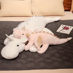 Pink and white dragon plush body pillows on a bed with a magazine nearby.