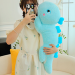 Woman holding a blue dinosaur plush with heart-shaped spikes, taking a photo with a smartphone.