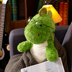 Green dinosaur plush wearing round glasses on a sofa with a blanket