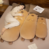 Woman lying on a bed with three tan capybara bolster pillows in different sizes