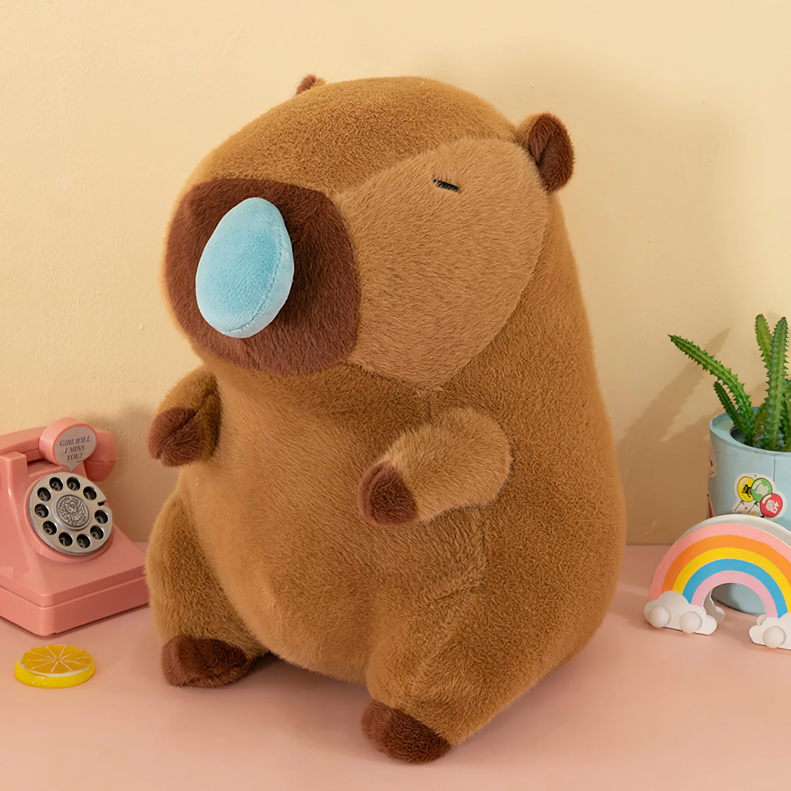 Brown sitting capybara plush with a blue nose bubble beside a pink telephone