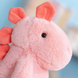 Close-up of a pink dinosaur plush face with a dark eye and coral ears