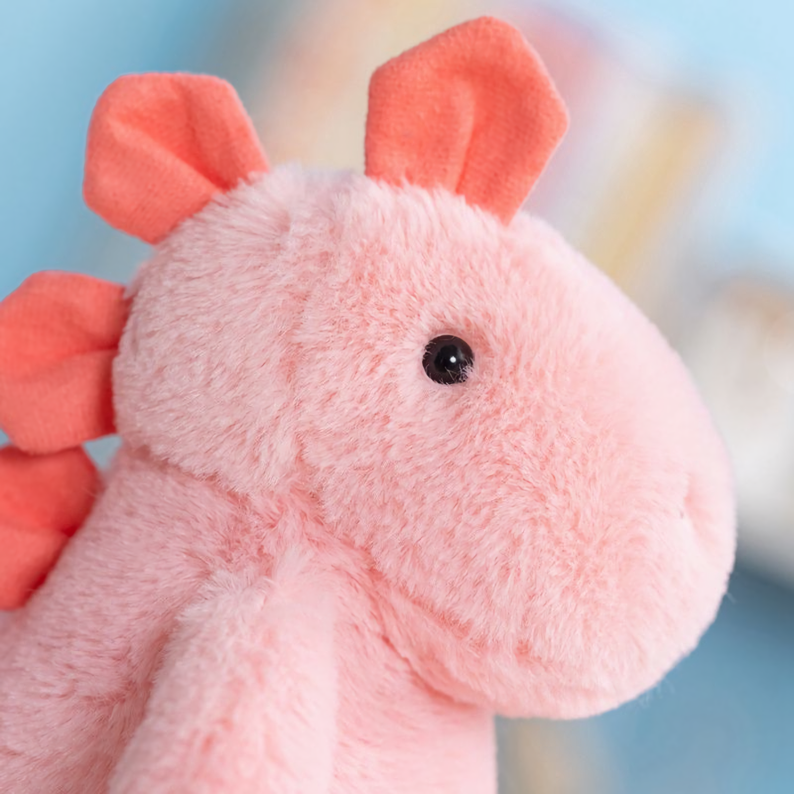 Close-up of a pink dinosaur plush face with a dark eye and coral ears