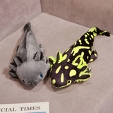 Gray axolotl plush and a black and lime green spotted axolotl plush on a gray sofa