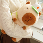 Arm holding a brown capybara plush with a white cap and a green strap