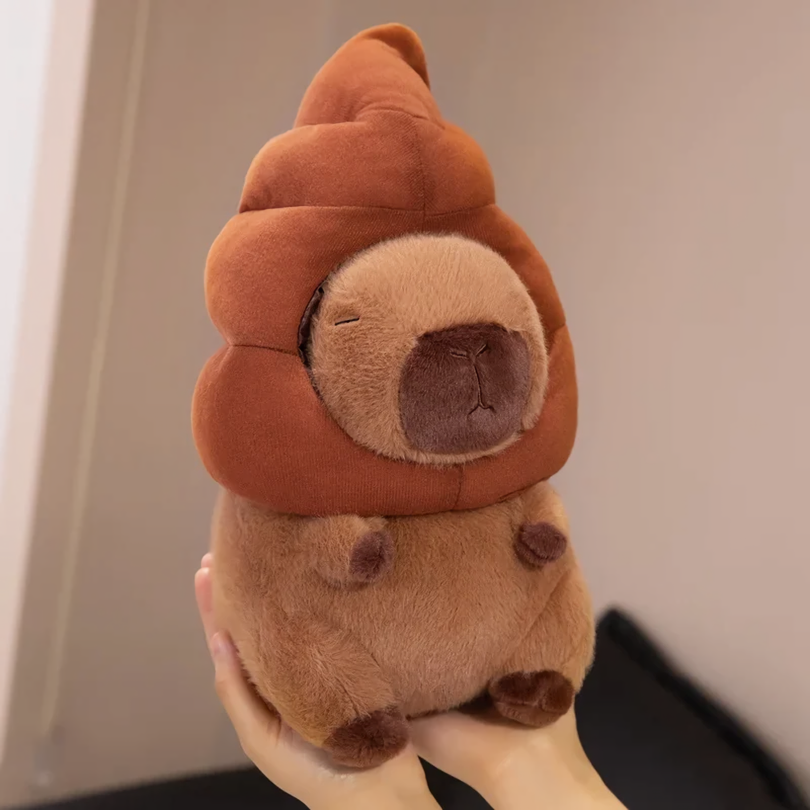 Hands holding a capybara plush with a brown swirl hat