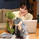 A woman smiling at green and gray T-Rex plush toys on a table next to a laptop and magazines.