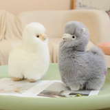 White and gray alpaca plushies on a green table beside a magazine