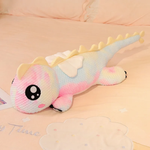 Rainbow pink dragon plush with big sparkly eyes and small wings on a pastel bed