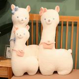 White alpaca plushies with pink bows and mini bags standing on a bed