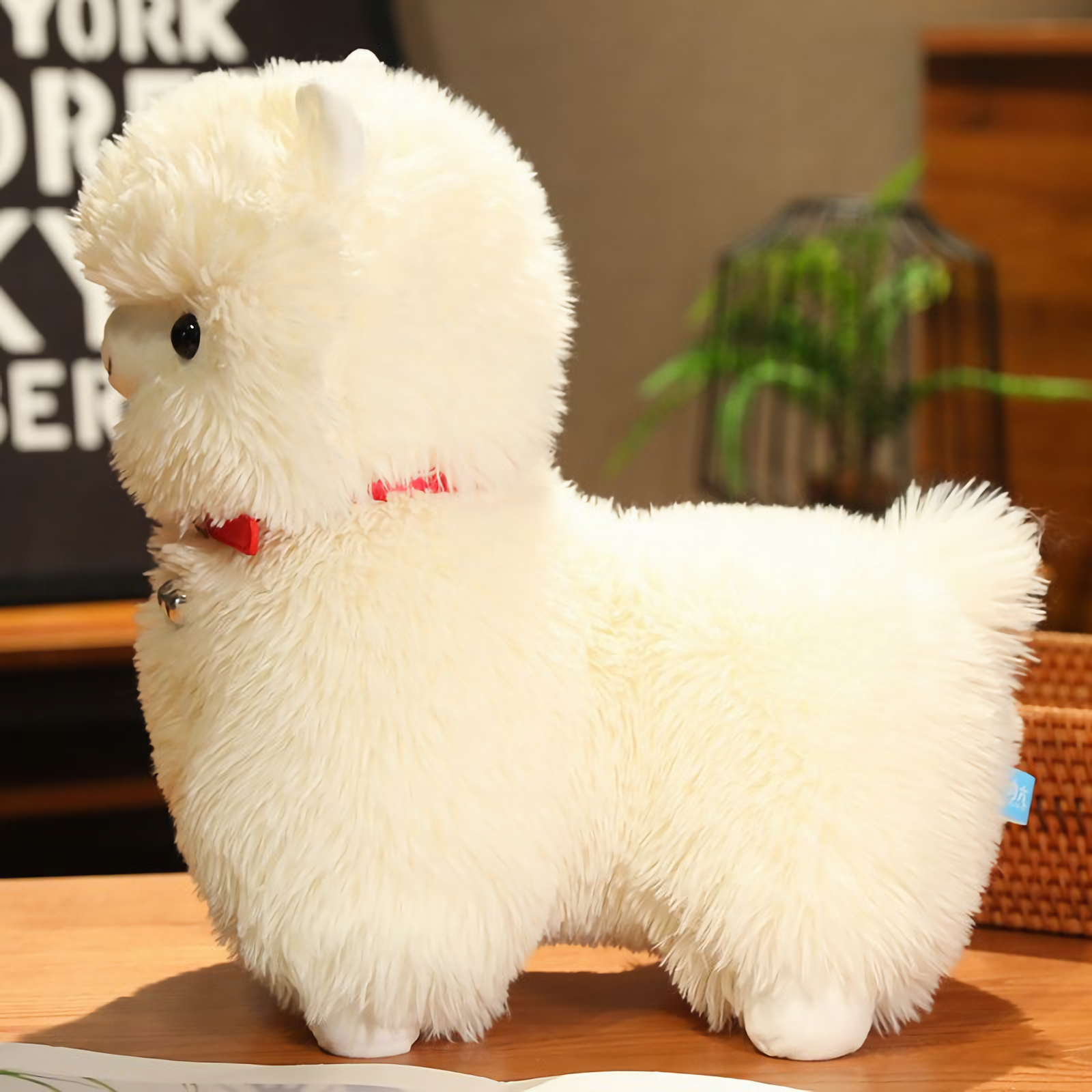 Side view of a white alpaca plush with a red collar sitting on a table