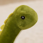 Close-up of green Brachiosaurus plush face with cream belly and yellow spikes, against a beige background.