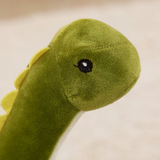 Close-up of green Brachiosaurus plush face with cream belly and yellow spikes, against a beige background.