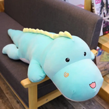 Blue dinosaur plush body pillow lying on a sofa with a cream ridge along its back