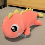 Pink dinosaur plush with yellow spikes, large eyes, and pink cheeks, lying flat on a bed.