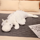 White dragon plush body pillow with horns and wings on a bed beside a magazine.