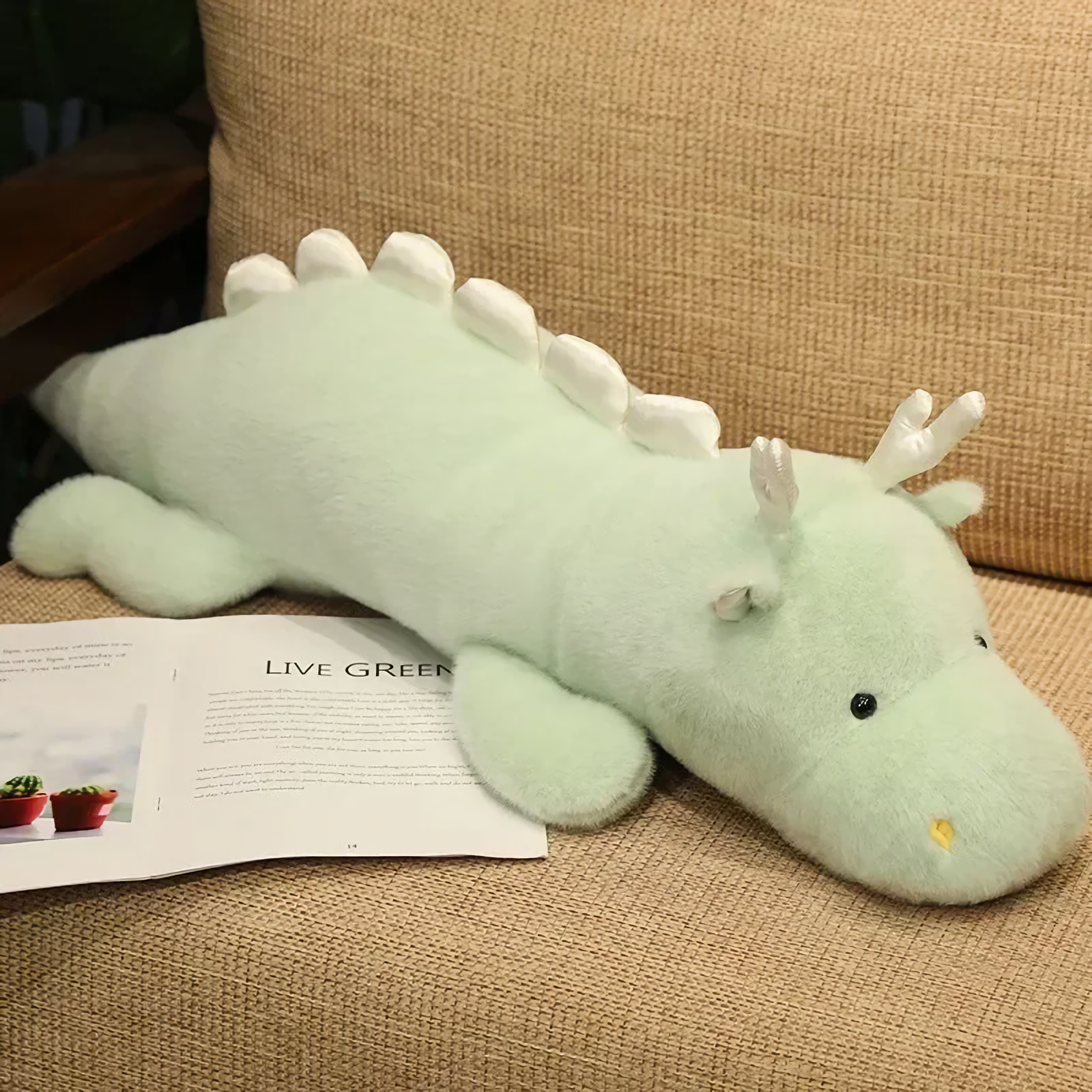 Mint green and white dragon plush body pillow on a sofa next to an open magazine.