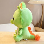 Green dragon plush with orange horns sits on a table, showing its side profile and orange-tipped tail.