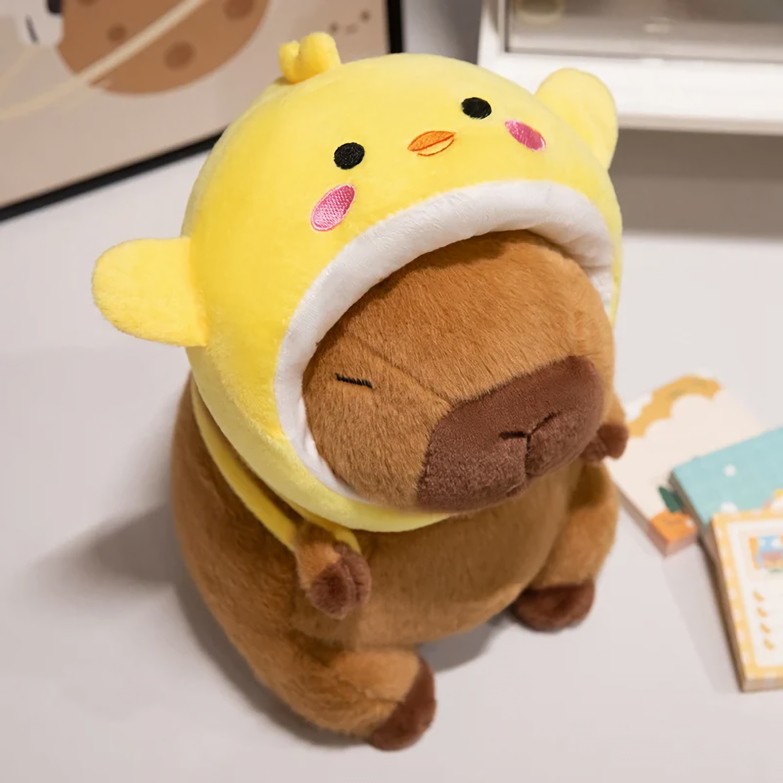 Capybara plush in a yellow chick hood on a white table