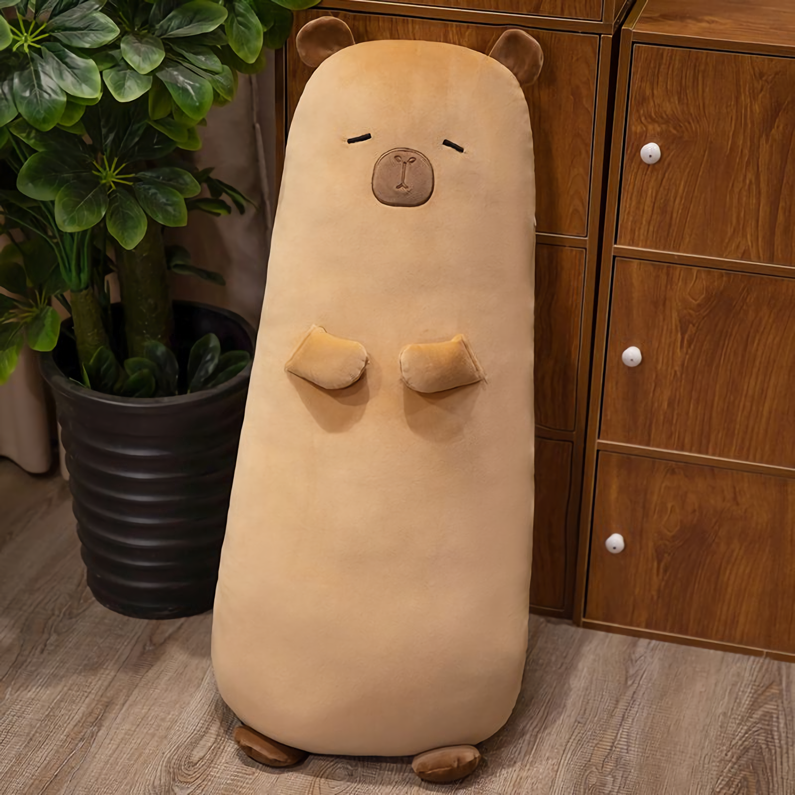 Tall tan capybara bolster pillow standing next to a wooden cabinet