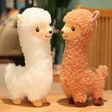White and brown alpaca plushies standing side by side on a bed