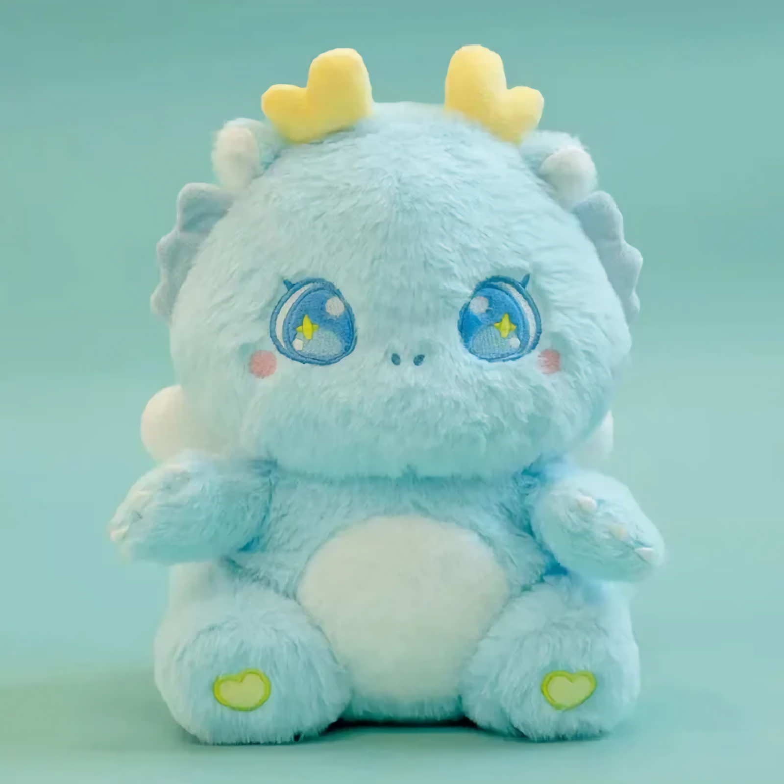 Blue baby dragon plush with golden horns and sparkly star eyes, sitting on a light blue background.