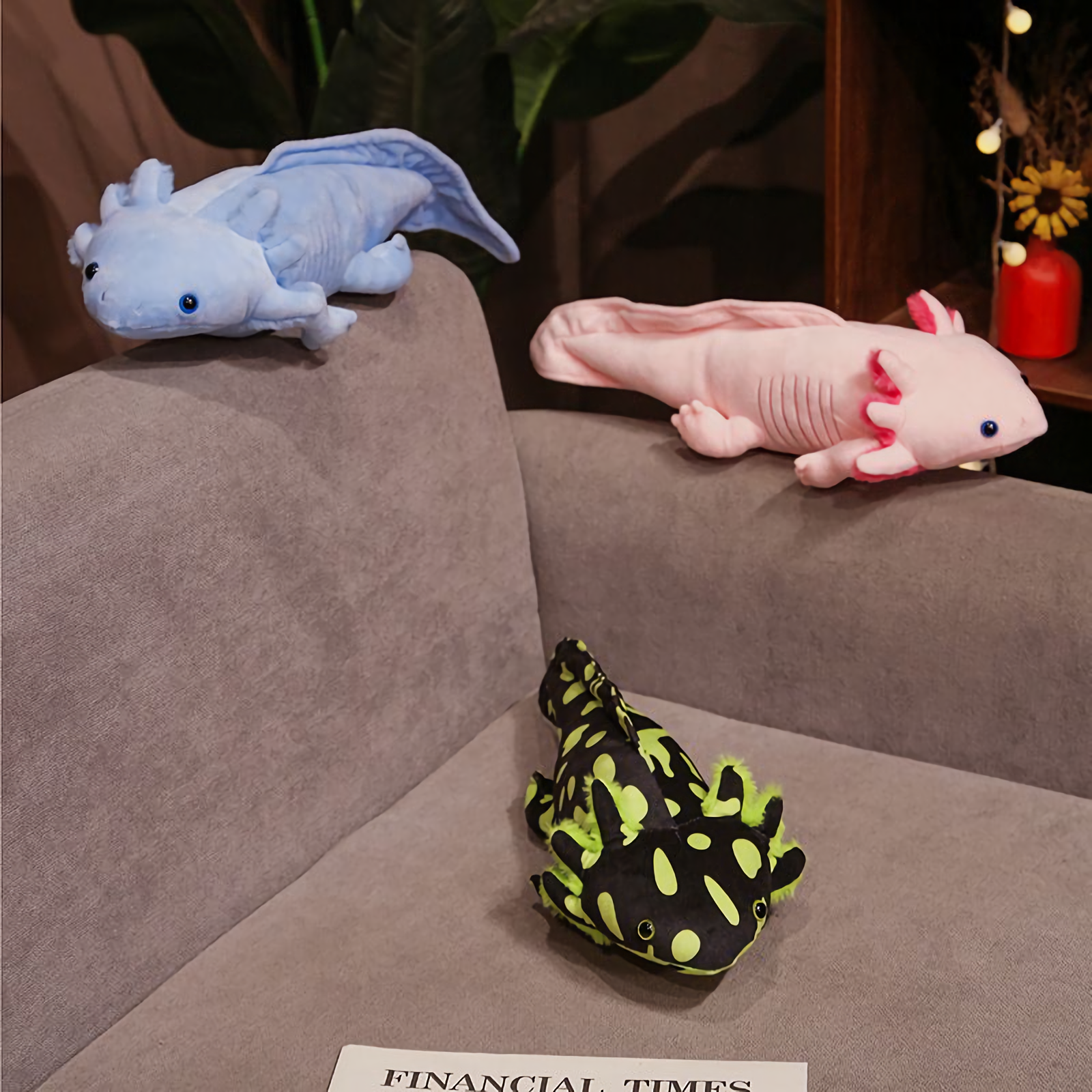 Blue and pink axolotl plushies and a spotted green one lying on a gray sofa